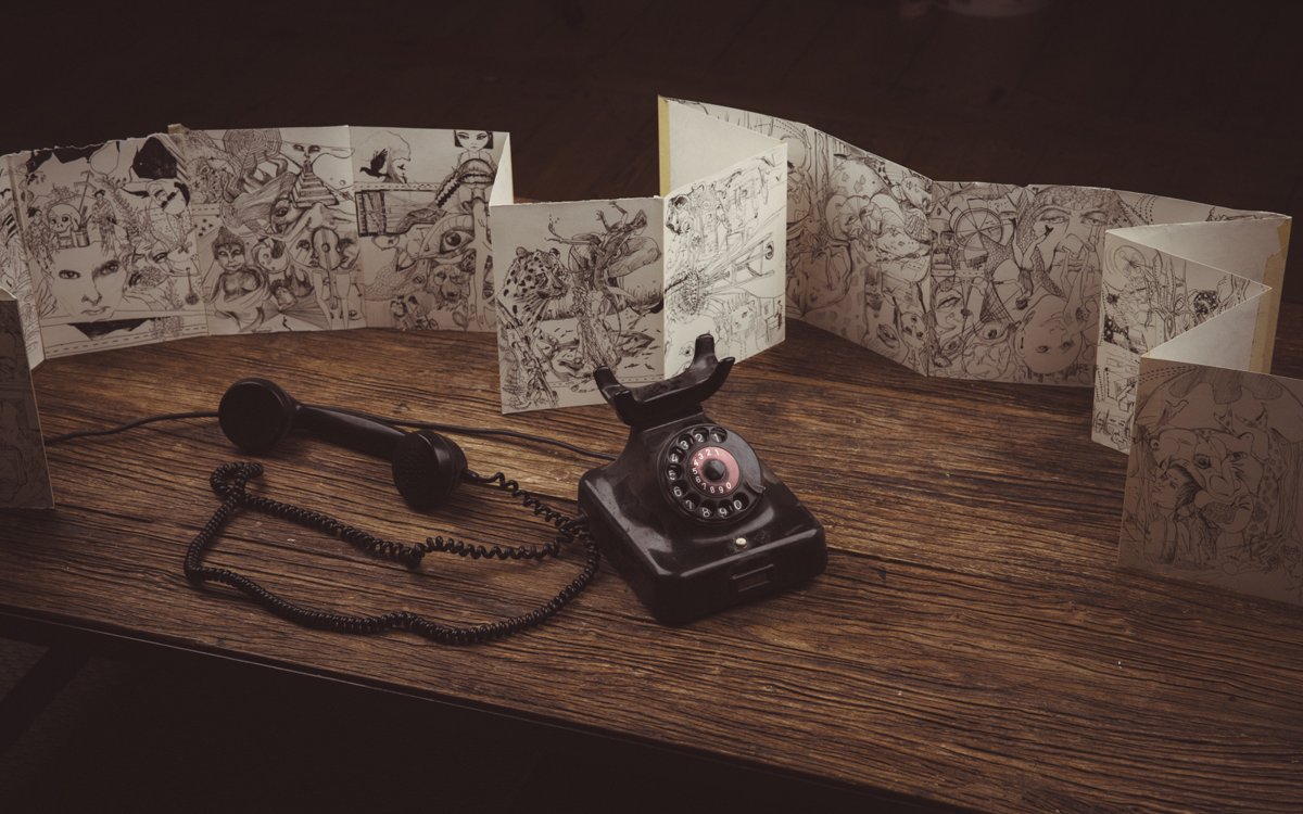 An old rotary telephone beside a folded sketchbook of drawings